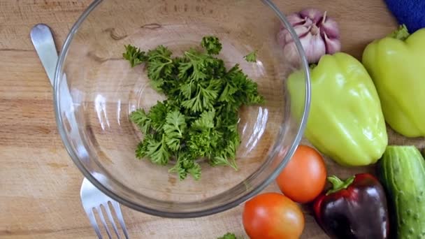 Le verdure fresche a fette sono sul tavolo, pronte per affettare l'insalata. Peperoncino bulgaro, pomodoro, erbe aromatiche, cetriolo, aglio per cucinare piatti di verdure. Un coltello e una forchetta accanto a una ciotola di vetro sul taglio — Video Stock