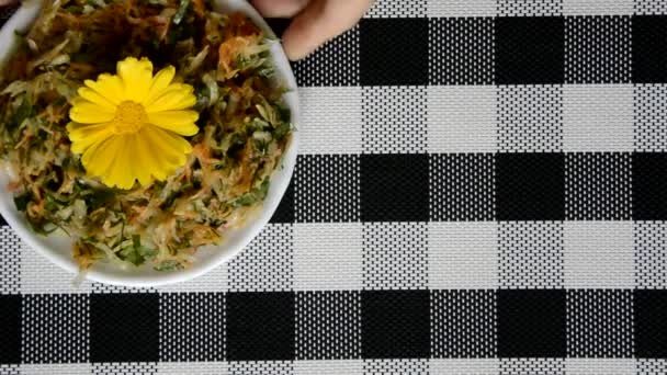 Checkered background in black and white. Hands put a plate of vitamin salad on the table. The salad is decorated with a marigold flower. — Stock Video