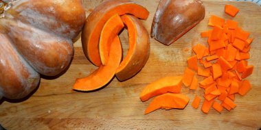 Masanın üzerinde olgun balkabağı parçaları yatıyor. Kesme tahtasında portakal rengi kocaman bir balkabağı. Diyet için vitaminler.