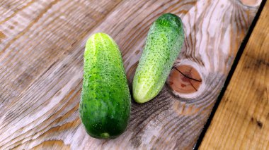 Tahta bir tahtanın üzerinde iki olgun yeşil salatalık yatıyor. Sebzeler yakın plan..