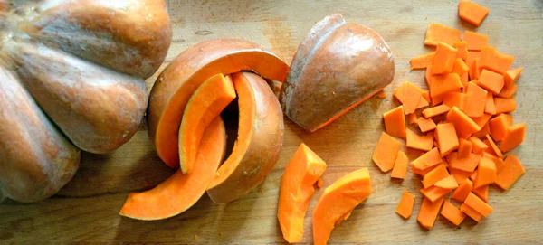 Kesme tahtasının üzerinde büyük ve küçük dilimler halinde kesilmiş olgun büyük balkabağı yatıyor..