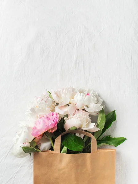 Bouquet of peonies in paper bag on white texture with copy space