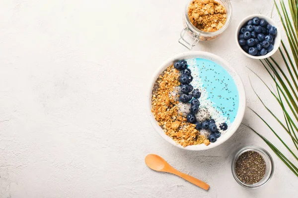 Blue smothie in bowl with granola and berries on white background