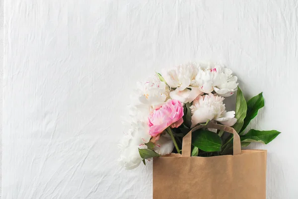 Bouquet of peonies in paper bag on white texture with copy space