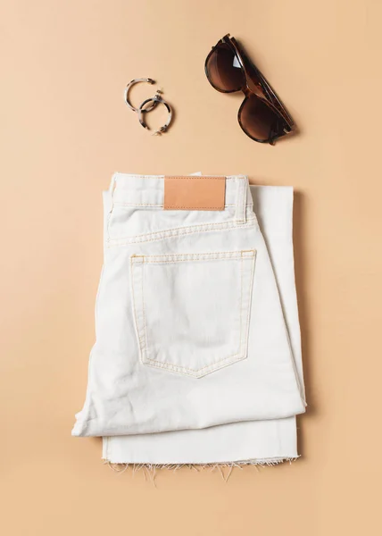 White jeans and denim fashion flat lay with accessories on beige