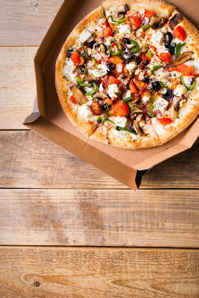 Delivery concept. Vegetable pizza in open cardboard box on woode