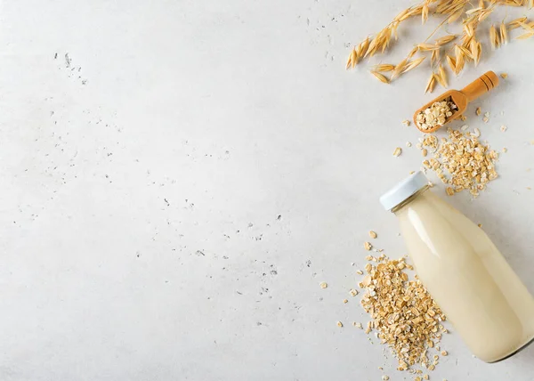 Oat milk in glass bottle with flakes and spike or ears of grain on white background, copy space