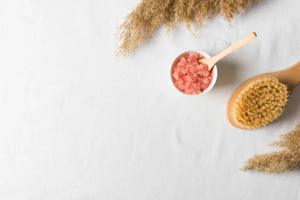 Nature cosmetic, scrub and brush with dry grass or flower on white texture background, flat lay, top view, copy space