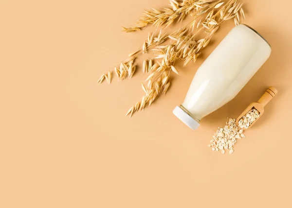 Oat milk in glass bottle with flakes and spike or ears of grain on beige background, copy space, top view,