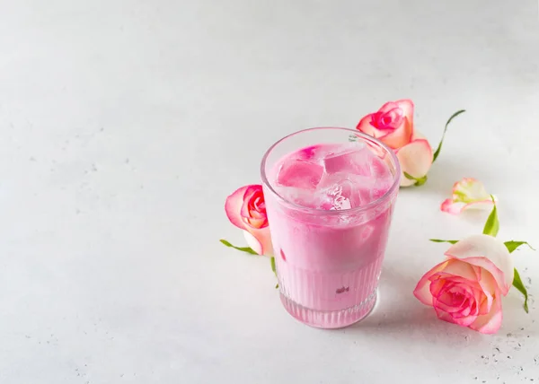 Ice rose latte in glass with pink flowers and petal on white or grey background, copy space