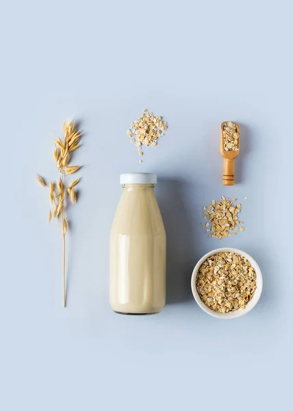 Oat milk in glass bottle with flakes and spike or ears of grain on blue background, knolling, copy space, top view,