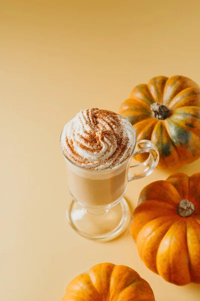 Spice pumpkin latte in glass with pumpkins on yellow background, copy space, top view, vertical