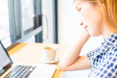 Güzel Asyalı kızlar iş, teknoloji ve (seçici odak ve yumuşak odak etkisi ile rahat kullanım için onun online iş yapmak uyandığımız kahve bir fincan ile dizüstü bilgisayar kullanan meşgul)