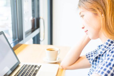 Güzel Asyalı kızlar iş, teknoloji ve (seçici odak ve yumuşak odak etkisi ile rahat kullanım için onun online iş yapmak uyandığımız kahve bir fincan ile dizüstü bilgisayar kullanan meşgul)