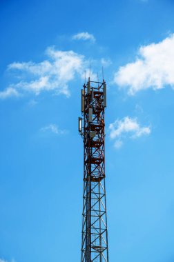 Mavi Gökyüzüne Karşı Yüksek İletişim Kulesi. Yüksek kalite fotoğraf. Mavi gökyüzünün altında, kabarık bulutlu modern bir iletişim kulesi. Teknoloji, altyapı ve iş görselleri için ideal..