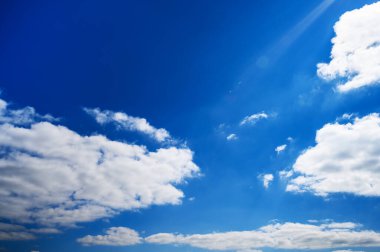 Güneş ışınları Bulutlu Mavi Gökyüzünü delip geçiyor. Yüksek kaliteli fotoğraf. Parlak mavi bir gökyüzünü, dağınık beyaz bulutlarla delen parlak güneş ışınları. Seyahat, doğa ve ilham verici arka plan görselleri için ideal..