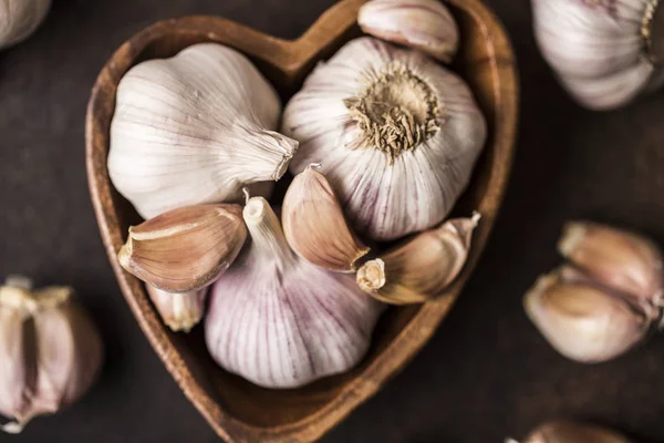 Garlic bulbs with garlic cloves in wooden bowl on dark background