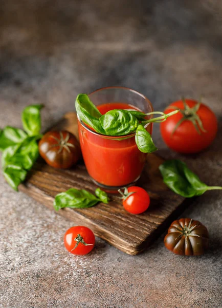 tomato juice in glass with herbs and green basil leaves with ripe red tomatoes on wooden background
