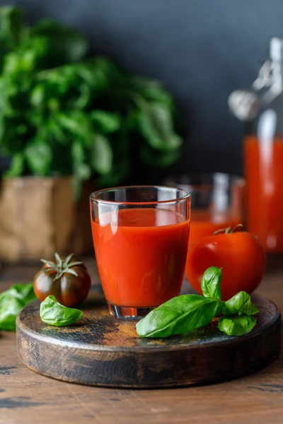 red tomato juice in glasses with herbs and green basil with ripe red tomatoes on wooden kitchen background, studio shot