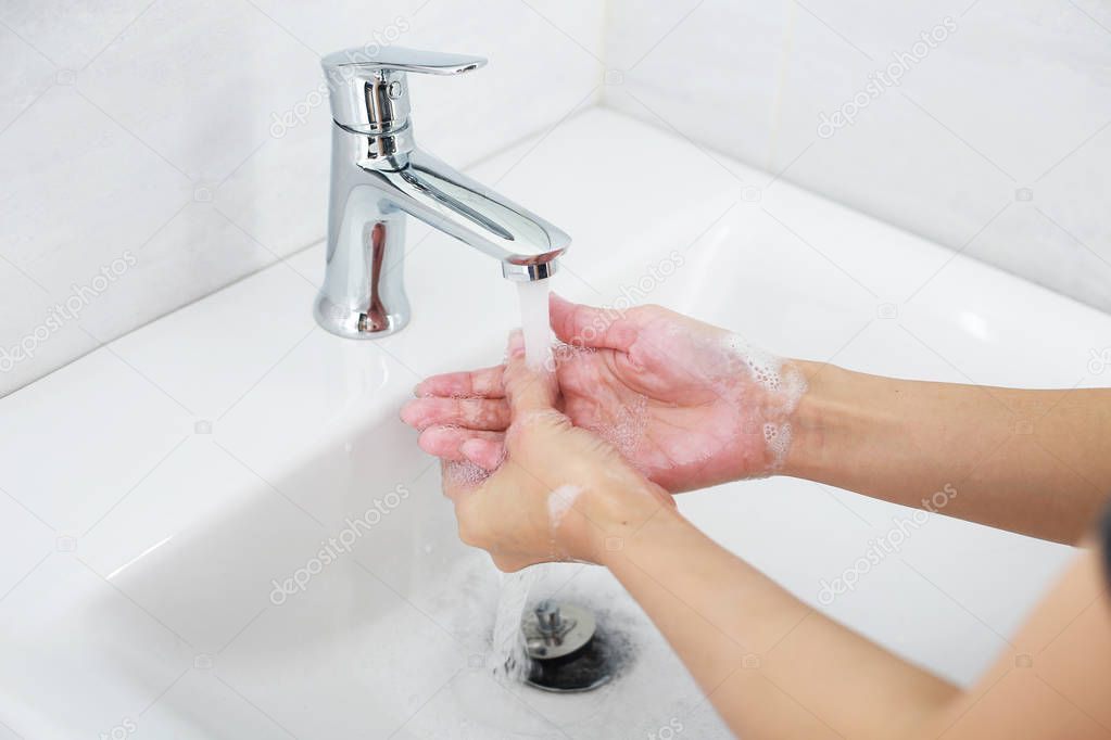 Washing hands with soap under the faucet with clean water.