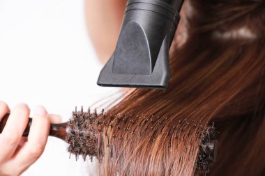 Güzel genç kadın bir saç kurutma makinesi kullanıyor.