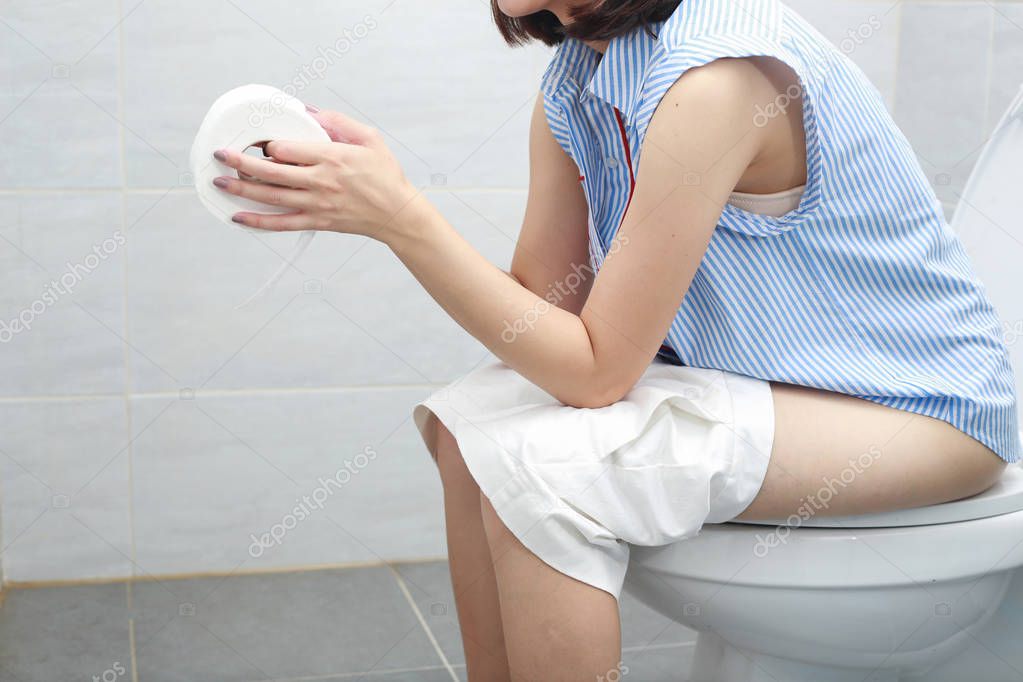 Woman in bath towel sitting on toilet bowl.