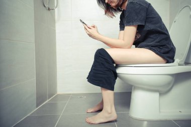 Sabah tuvalette akıllı telefon kullanan kadın.