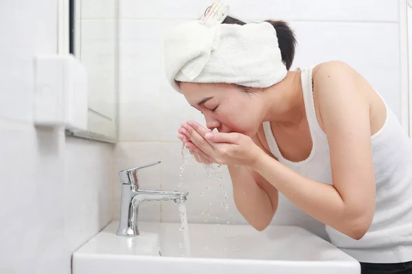 Hermosa joven lavándose la cara salpicando agua en un baño — Foto de Stock