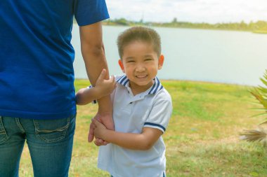 Baba ve oğul parkta mutlu gülümseyerek el ele tutuşuyor.