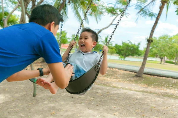 Pai e filho tendo engraçado no balanço no playground . — Fotografia de Stock