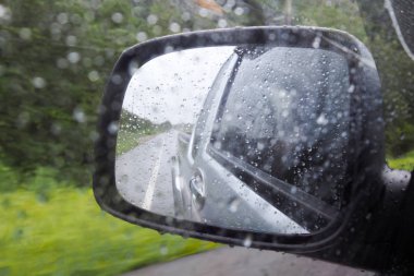 Yağmurlu bir günde yolda sürüş sırasında kanat ayna veya arabanın dış ayna üzerinde yağmur damla. Kazayı azaltmak için yağmurlu günde dikkatli sür.