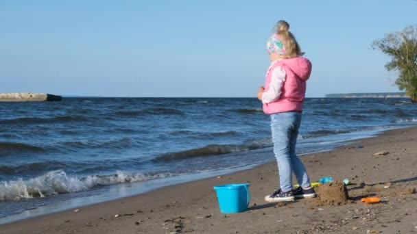 可爱的小女孩在沙滩上玩慢动作 沿着海滩散步的小女孩小女孩在海边独自慢慢地走着 孩子在沙滩上的海浪上散步 — 图库视频影像