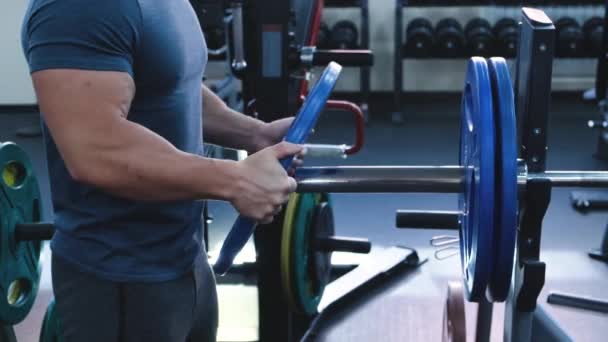 手のクローズアップ ボディビルダーは バーベルに追加の重量を置きます ハードコアガレージジム施設での筋肉フィットの人々のトレーニング 重い重量を持ち上げる — ストック動画
