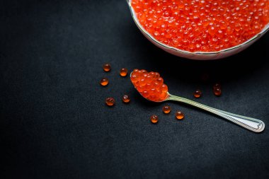 Kırmızı havyar kaşıkta. Siyah arka plan üzerinde havyar kasesi. Yakın plan somon havyarı. Deniz ürünleri. Lezzetli. Gurme yemeği. Havyar dokusu.