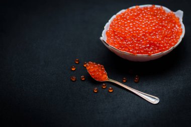 Kırmızı havyar kaşıkta. Siyah arka plan üzerinde havyar kasesi. Yakın plan somon havyarı. Deniz ürünleri. Lezzetli. Gurme yemeği. Havyar dokusu.