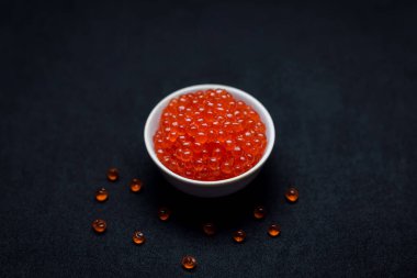 Kırmızı havyar kaşıkta. Siyah arka plan üzerinde havyar kasesi. Yakın plan somon havyarı. Deniz ürünleri. Lezzetli. Gurme yemeği. Havyar dokusu.