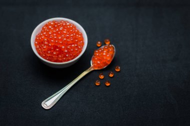 Kırmızı havyar kaşıkta. Siyah arka plan üzerinde havyar kasesi. Yakın plan somon havyarı. Deniz ürünleri. Lezzetli. Gurme yemeği. Havyar dokusu.