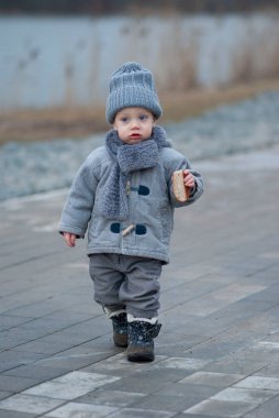 Üzgün çocuk elinde bir parça ekmekle nehir kıyısında yürüyor.
