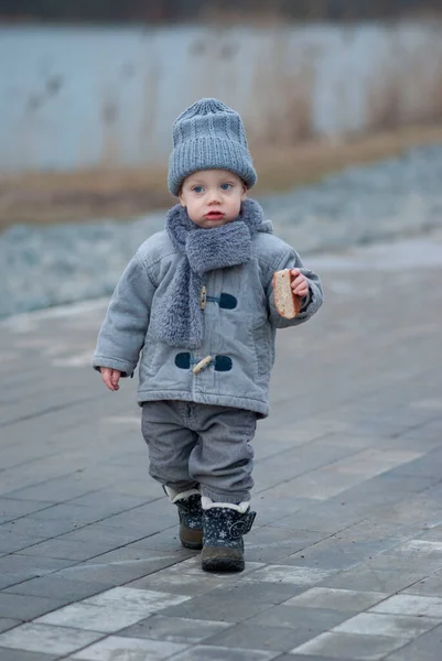 Üzgün çocuk elinde bir parça ekmekle nehir kıyısında yürüyor.