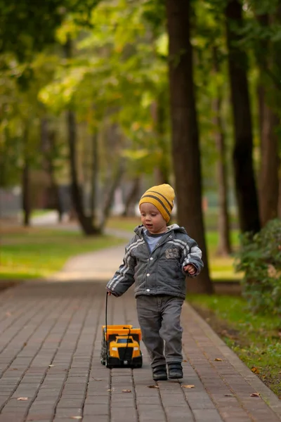 Küçük çocuk, parkta yol boyunca bir ipe oyuncak bir araba sarar.
