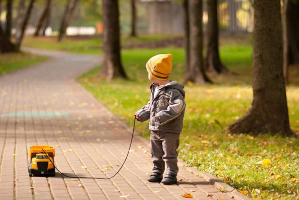 Küçük çocuk, parkta yol boyunca bir ipe oyuncak bir araba sarar.
