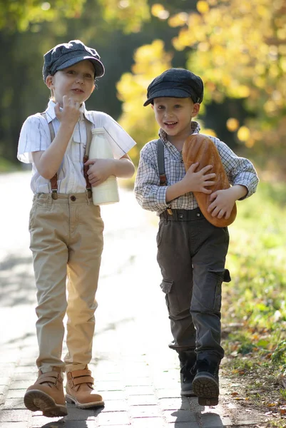 Köylü çocuklar bir şişe süt ve kolunun altında somunla yol boyunca yürüyorlar.