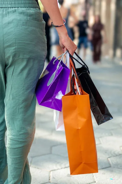 Zevkli alışverişlerle dolu başarılı bir alışveriş çılgınlığının tadını çıkardıktan sonra neşeli bir şekilde şehir caddesinde yürüyen bir kadın.