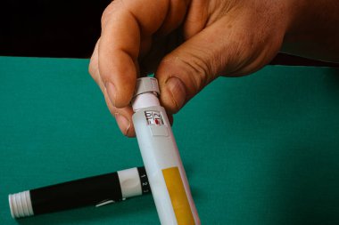 Ensülin kaleminde doğru dozu arayan bir eli kapatın, günlük diyabet ve kronik hastalıkların kendi kendine enjekte edilen enjeksiyonlar yoluyla yönetildiğini vurgulayın