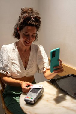 NFC teknolojisiyle ödeme yapan gülümseyen müşteriler bir mağazadaki pos terminalinde, kredi kartı tutuyor, modern ve uygun alışveriş deneyimlerinin tadını çıkarıyor.