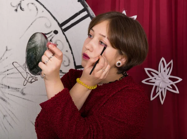 The girl puts makeup on her eyes in front of a mirror on the background of New Year\'s watches