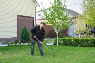 Bir adam yazlık evinde yeşil çimenlik üzerinde eski yeşillik tırmıklar