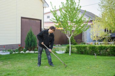 Bir adam yazlık evinde yeşil çimenlik üzerinde eski yeşillik tırmıklar