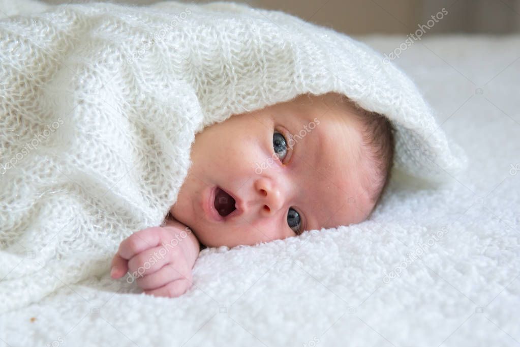 Newborn baby lies on a white plaid, covered with a knitted shawl
