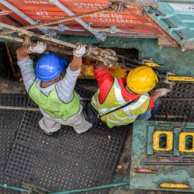 PASIR GUDANG, MALAYSIA - Feb 02, 2017: Longshoremen uses long rods with turnbuckles to secure containers on an container ship in deck sockets. clipart